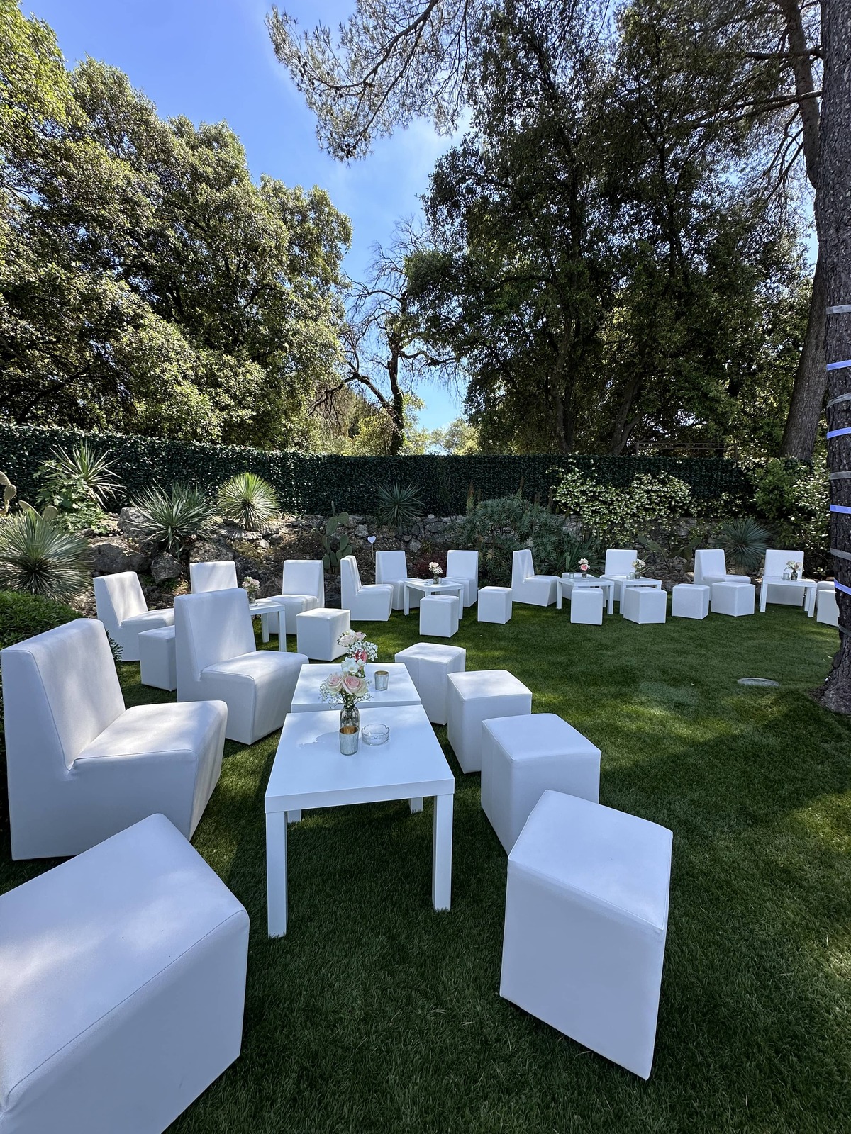 Table basse événementielle blanche entourée de fauteuils et poufs assortis, disposée en espace lounge extérieur ou intérieur, pour réceptions, mariages, anniversaire et événements sur la Côte d’Azur Agence évènementielle loueur de mobilier